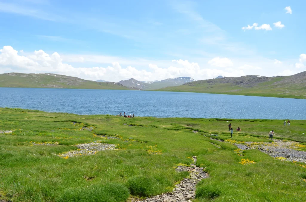 Deep blue Sheosar Lake ringed by green meadows and snow-streaked ridges at 4,250 m