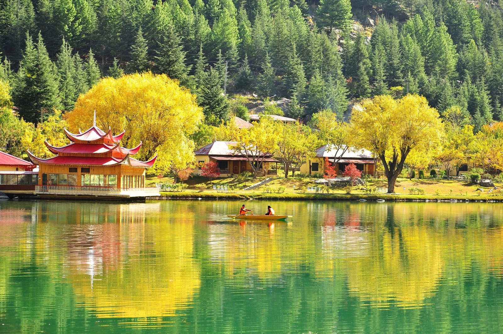 A small boat on the green water of Lower Kachura Lake with pine-covered slopes behind