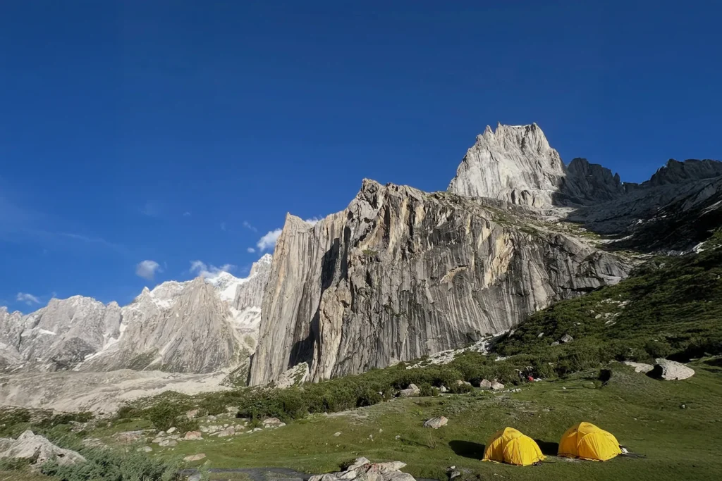 Trekkers camp in a green meadow below granite towers with a glacial stream