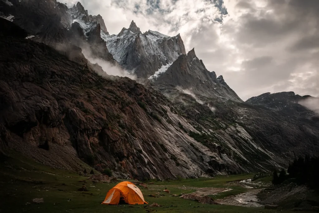 Orange expedition tent in a meadow below jagged rock spires