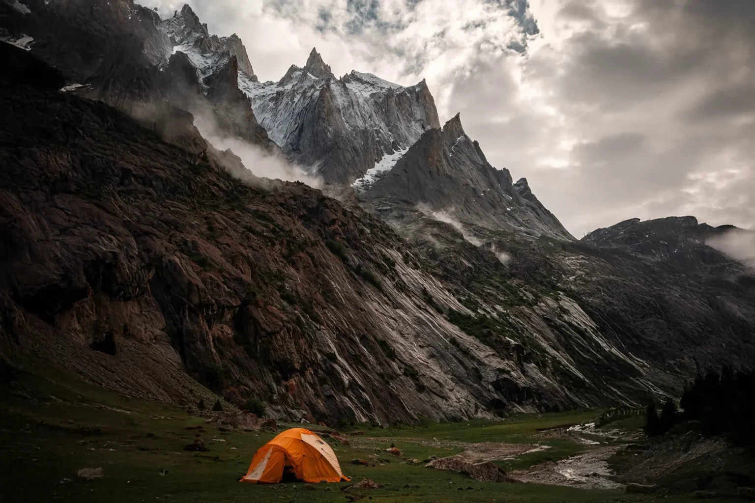 Orange expedition tent in a meadow below jagged rock spires