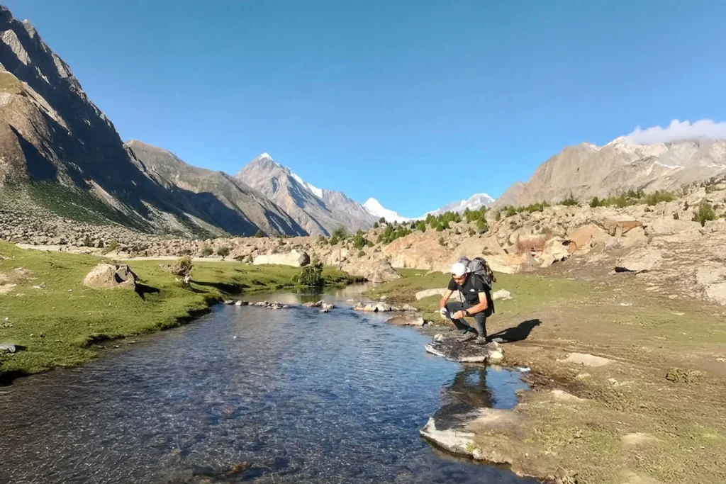Trekker crossing a meadow stream on the way to high camp