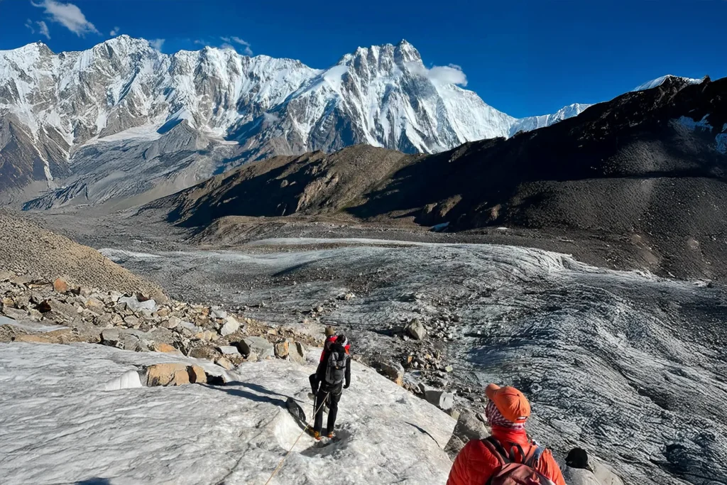 Rope team of trekkers on a glacier below a giant Karakoram peak