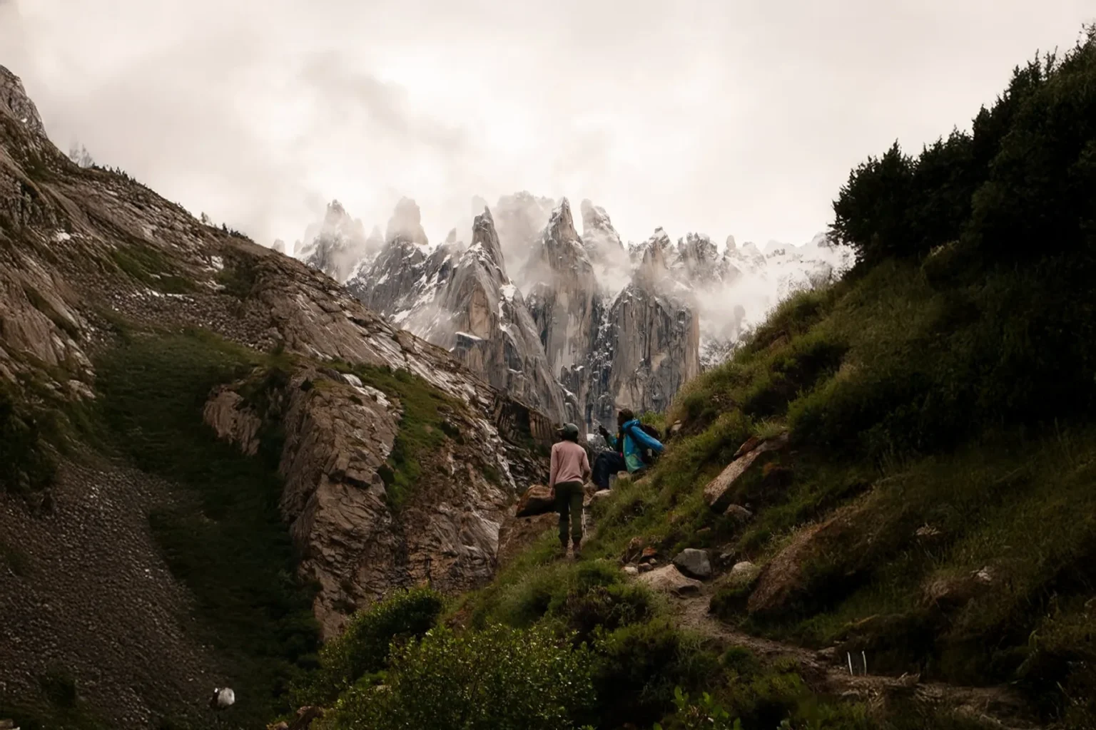 Trekkers on a green trail walking toward granite spires
